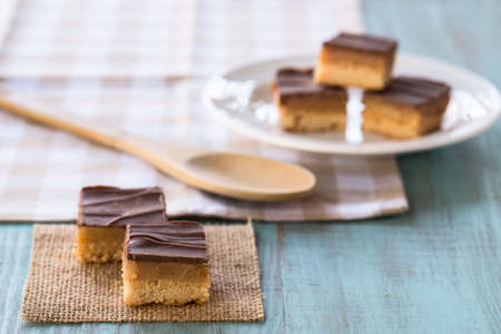 Chocolate and caramel candy cookies Millionaire Bars with wood spoon on checkered napkinの写真素材