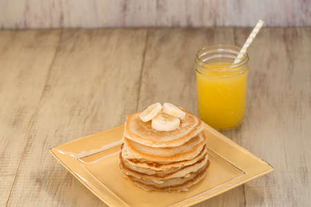 A stack of tasty breakfast pancakes with bananas and a glass of fresh squeezed orange juice