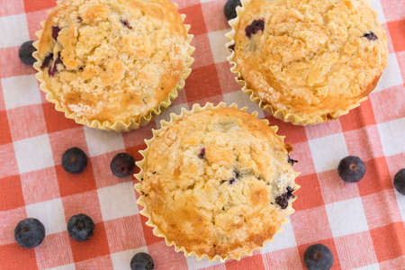 Blueberry muffins for breakfast on orange checkered napkin with berries scattered