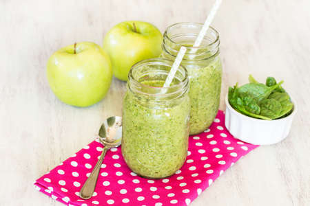 Green fruit and vegetable spinach vegan smoothies on pink dotted napkin with apples and bananaの写真素材