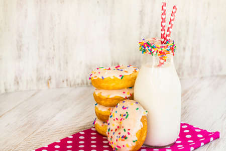Breakfast snack of cake donuts with sprinkles and glass of milk on white wood backgroundの写真素材