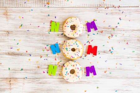 Nom Nom Nom silly donut saying on white wood background with colorful sprinkles and lettersの写真素材