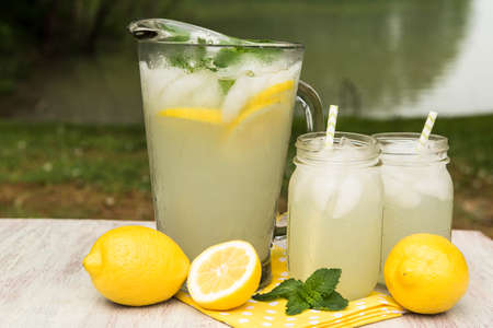 Glass pitcher and mugs of lemonade with lemons and mint outside by the lake in summerの写真素材
