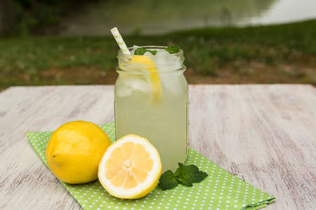 Glass of tasty lemonade with lemons and mint sprigs outside by the lake in summerの写真素材