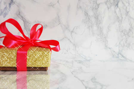 golden gift with red ribbon on marble tableの写真素材