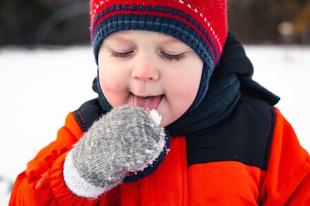 Adorable baby boy eat cold snow from mittens in winter parkの写真素材