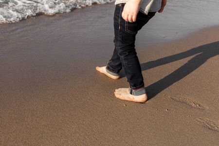 Kid's feet standing on the beach near by the sea.