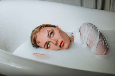 Beautiful young sexy girl with blonde hair wet, exotic makeup, takes bath with milk tan perfect skin, beauty cosmetic salon and spa for woman.の写真素材