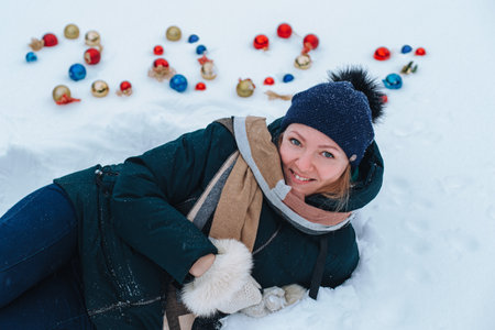 girl lies on the white snow. Behind her are the numbers 2021 made of Christmas tree decorations.の写真素材