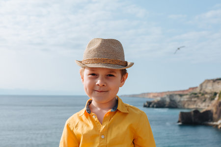 portrait of a boy 4-7 against the background of mountains and the sea. He is wearing a yellow shirt...