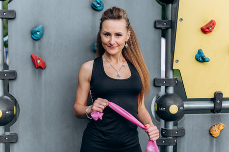 Portrait of a slender fitness girl stands and stretches the elastic band with her hands against the...
