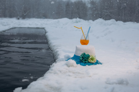 Winter swimming in a lake in an ice hole on a frosty day. A glass with a drink and a straw hat near the ice hole.の写真素材