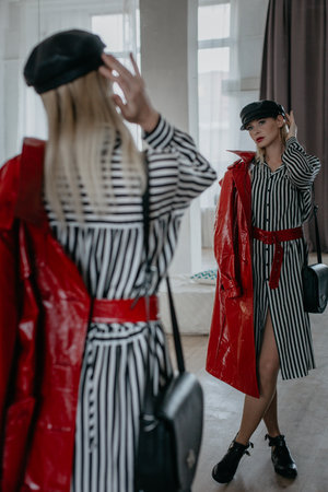 A Chic Woman Dressed in a Stylish Striped Dress and Bold Red Coat, Reflecting in a Mirrorの写真素材