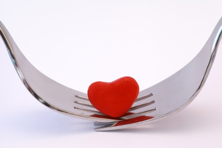 Symbolising romantic meal for two with two forks and a red heart on a white background.の写真素材