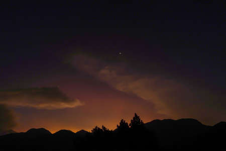 Sunset panoramic view from top of mountain peak with yellow moon silhouette on background of sky...