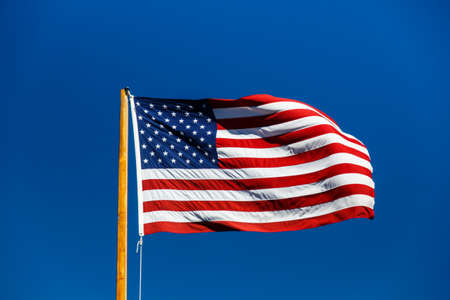 American flag with stars and stripes fluttering in blue skyの写真素材