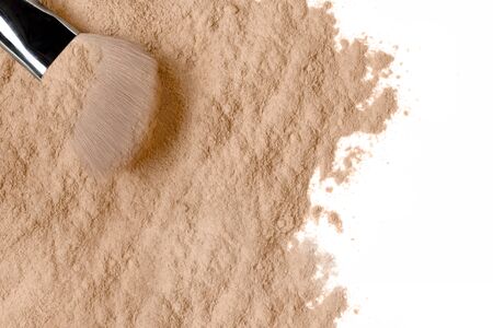 Loose cosmetic powder scattered on a white background with soft bristle makeup brush in a...