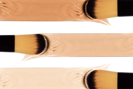 Color swatches of liquid foundation over a white background in a beauty, makeup and cosmetology concept. Makeup brushes in close-up applying liquid foundation. Isolated on whiteの写真素材