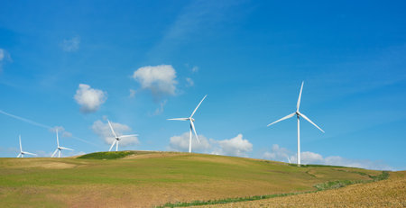 Windmill energy transformation. Windmill turbines across picturesque landscape with green grass...