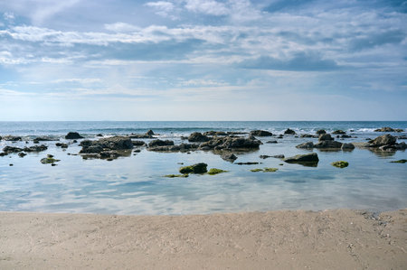 Sand and rock beach against the blue sky with stratocumulus clouds. Valdevaqueros Beach, Tarifa, Cadiz, on the Atlantic Ocean coastline. Seascape of the Andalusian coast in Spainの写真素材