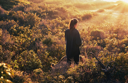 Woman walking with her German Shepherd dog in coastal dune vegetation as the dog looks back at the...