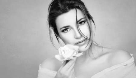 Monochrome beauty portrait of a beautiful woman with a flawless healthy skin holding a fresh white rose to face. Youth and skin care conceptの写真素材