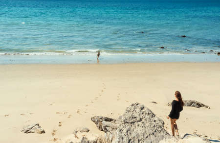 Young woman walking towards the ocean along the sand of the dune on a tropical beach, while her...