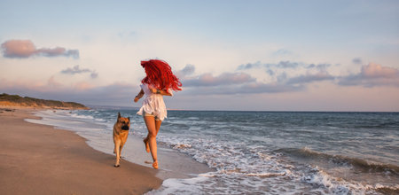 Carefree fit body girl enjoys her holidays running with her German shepherd dog at tropical paradise beach. Happy red-haired woman on travel vacation. Friendship, fun and enjoyment at summer vacationの写真素材