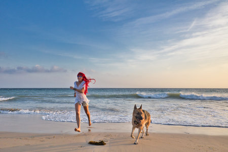 Happy red-haired woman in casual summer style running on the beach with her dogの写真素材