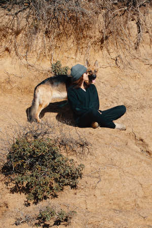 German Shepherd dog enjoying communication with her owner sitting on a sandy cliff while relaxing in...