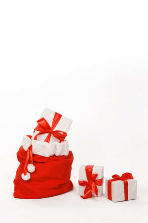 Christmas card with Santa's bag full of presents next to two other gift boxes wrapped in white paper and decorated with red ribbon against white studio background for copy spaceの写真素材