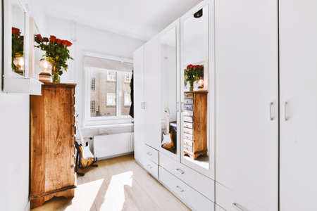 White wardrobe with mirrors located near guitar and cabinet in light room at home