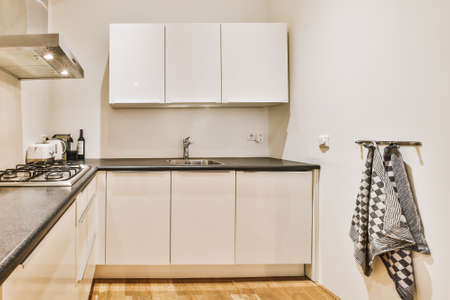 Fragment of interior of light narrow home kitchen with minimalist style white furniture with sink and stoveの写真素材