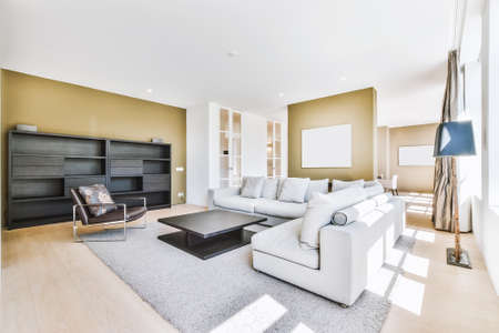 Stylish home interior design of spacious living room with large windows and white walls furnished with comfy couch and table on carpet on parquet floorの写真素材
