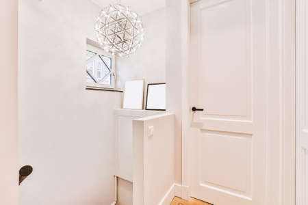 Closed white door of room located near framed pictures and stylish lamp on top of stairway at home