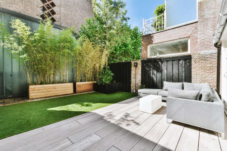 Comfortable couch placed on terrace near bamboo plants outside brick house on sunny summer day