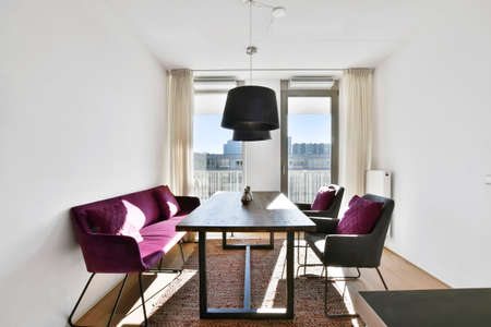 Comfortable chairs with cushions and sofa located near table under lamps in stylish dining room in...