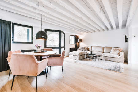 Open plan black kitchen in white living room with dining table and gray sofa