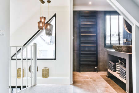 Modern apartment hall with staircase fence and open access to bathroom with dark tile and window