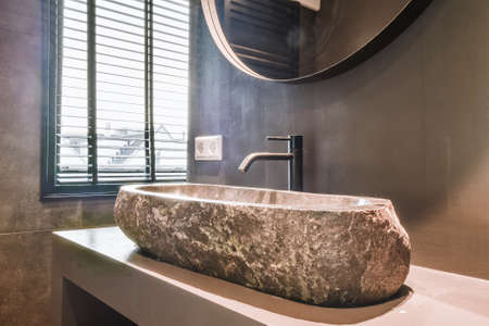 Expensive vessel sink made of natural stone with black faucet under mirror in bathroomの写真素材