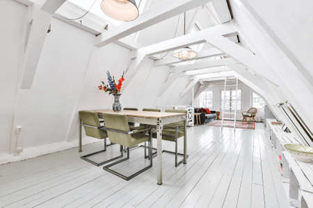 Interior of attic studio apartment with roof beams furnished with dining table and sofa in living roomの写真素材