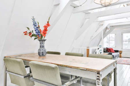 Country wooden table with green chairs and vase of flowers on top in studio apartment on attic levelの写真素材