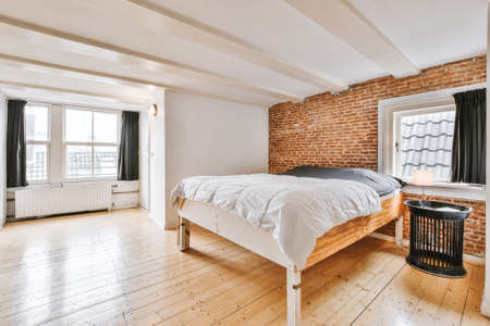 Stylish simple interior of bedroom with brick wall and wooden bed under white ceiling with beams