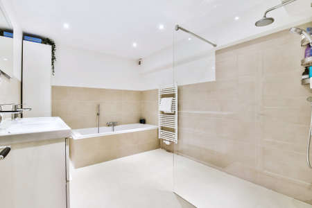 Contemporary bathroom with bathtub and glass shower cabin with light beige tile and white ceiling