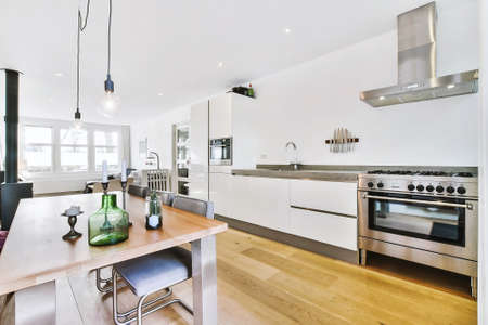 Modern open plan kitchen with white cabinets and dining table in studio room with sofa and fireplace