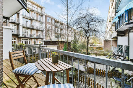 Balcony of apartment with wooden chairs and table viewing town with spring trees in sunny day