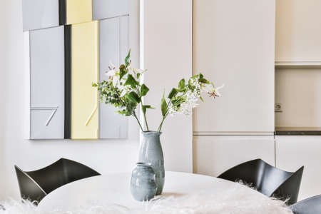 Ceramic vases with blooming branches placed on table near chairs in stylish dining room at homeの写真素材