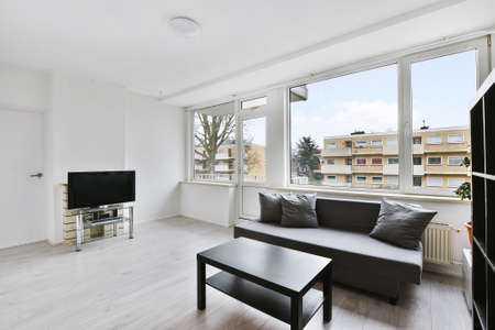 White living room with gray couch and black coffee table and TV with bare windows viewing...