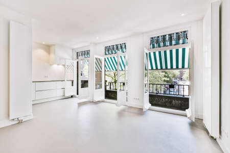 Interior of spacious light room with doors opened to balcony with canopy on sunny summer day