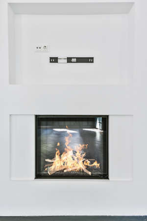 Modern electric fireplace with glass screen installed in white wall in living roomの写真素材